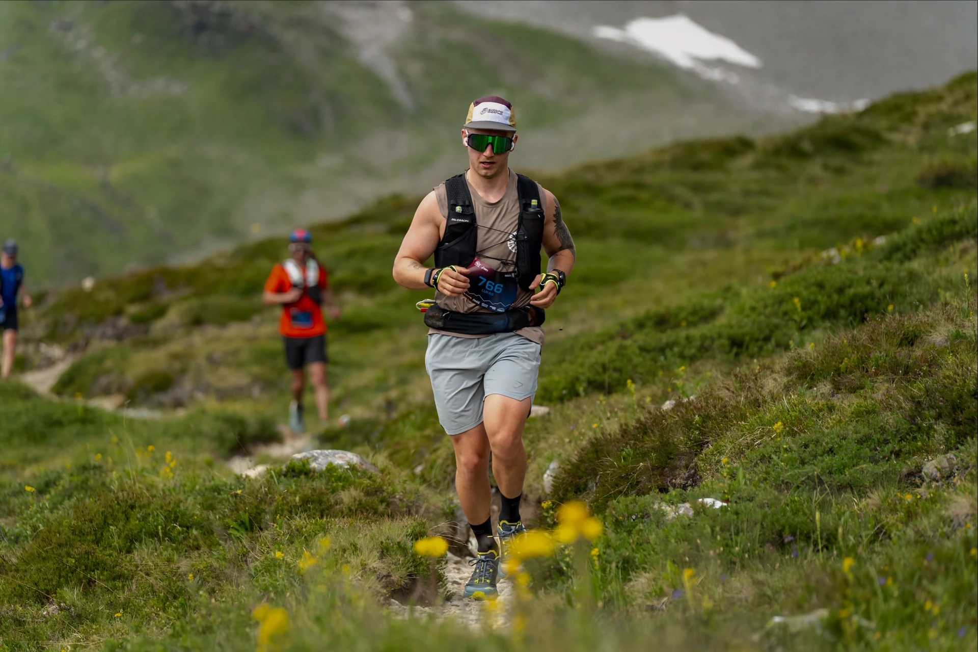 Lukas Ludl beim Trailrunning auf einem schmalen Pfad durch grüne Berghänge.